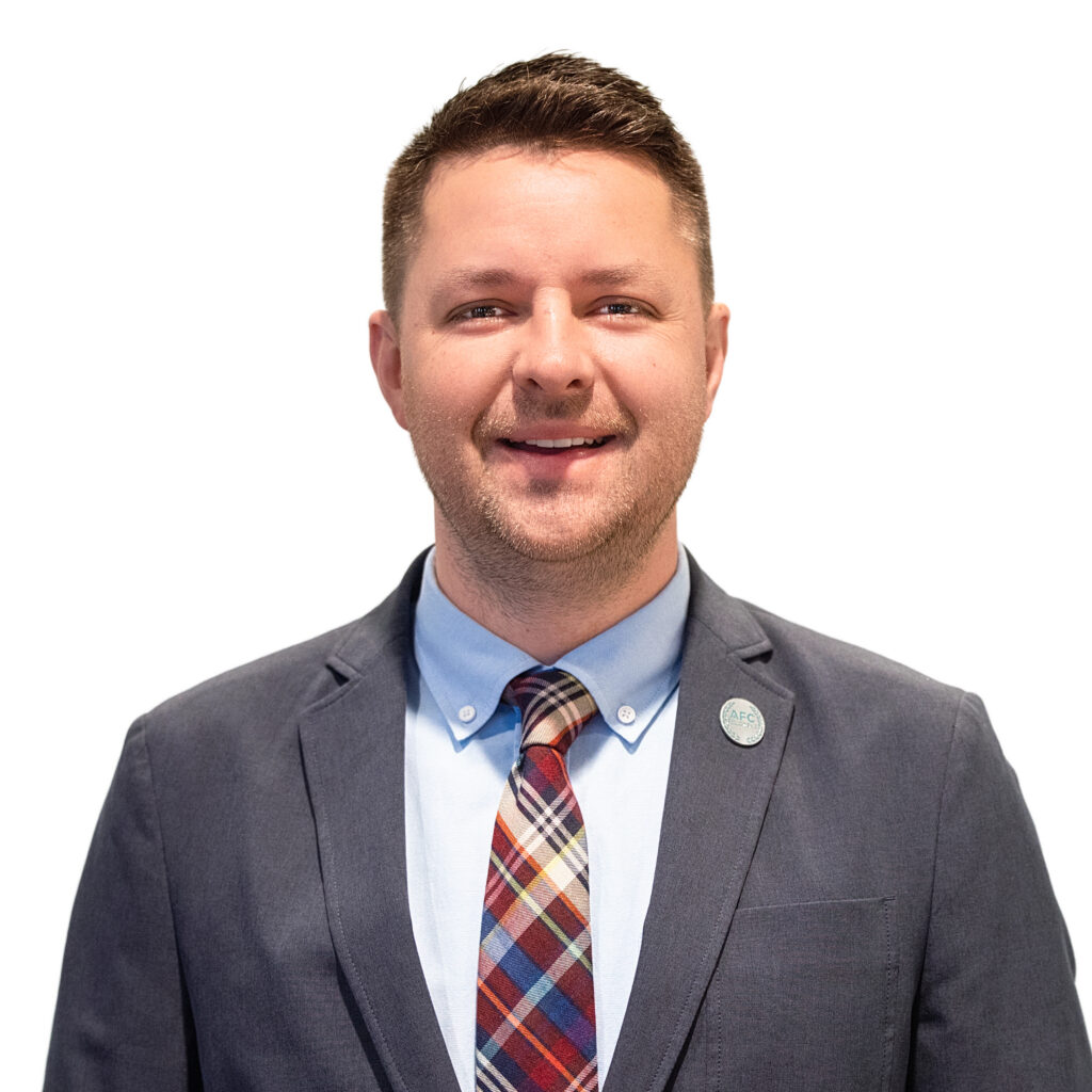 Man in gray blazer and blue shirt with a tie looking at camera